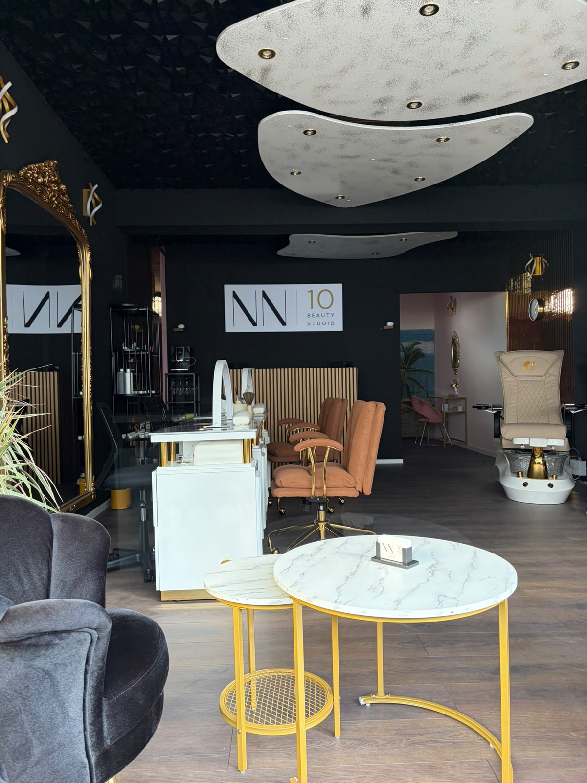 Blick in das NN10 Beauty Studio — beleuchtetes Logo an schwarzer Wand, Maniküre-Tische mit Marmorplatten und Pediküre-Sessel im Hintergrund